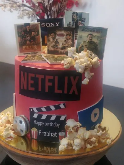 A Netflix and chill themed cake for a movie and series lover. The cake is decorated with edible posters of shows like Mirzapur and movies like Avatar, complete with popcorn.