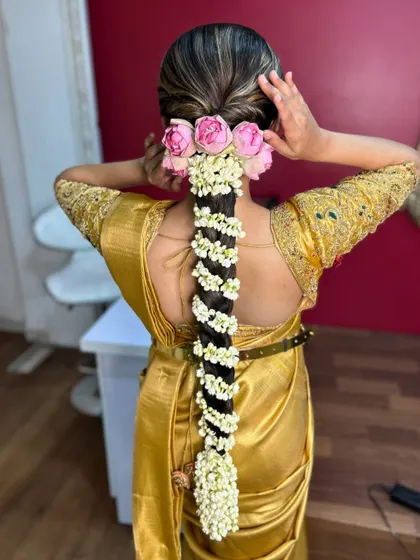 A bride adjusting her hair, showing a beautiful traditional braid with pink roses and jasmine flowers, a perfect look for a South Indian wedding.
