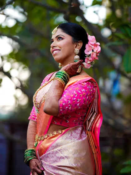 A portrait of the bride looking up with a happy smile, her pink and gold saree glowing in the natural light.