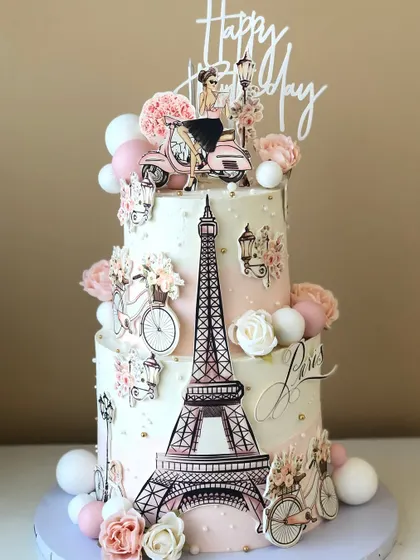 A chic, two-tiered Paris-themed cake, perfect for a fashionista. It's decorated with the Eiffel Tower, a scooter, and floral details.