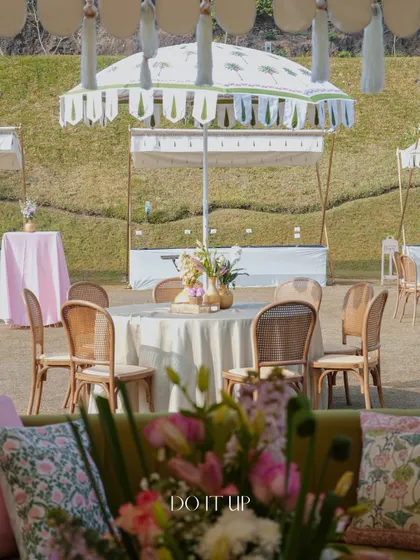 A beautiful outdoor lunch setup in Udaipur, featuring tables shaded by custom-printed umbrellas. The cane-back chairs and soft-colored linens create a relaxed yet sophisticated daytime look.
