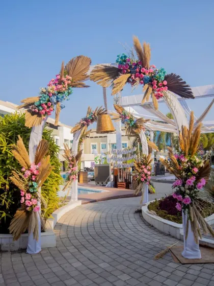 A beautiful bohemian-style entrance arch for a poolside carnival, decorated with dried palm leaves, pampas grass, and colorful flowers.
