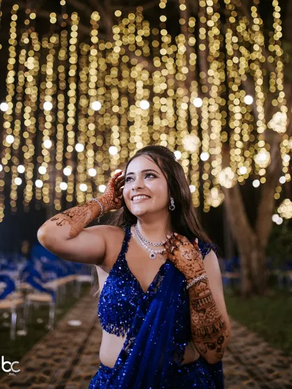 A joyful upward glance from the bride, with her intricate mehendi framing her face and a beautiful bokeh of fairy lights in the background.