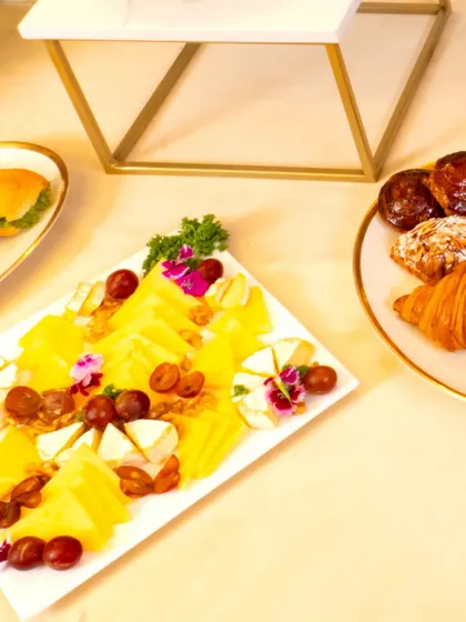 A delightful cheese platter served alongside fresh pastries from L'Opéra. The board is garnished with edible flowers, grapes, and nuts, creating a perfect pairing for a high-tea event.