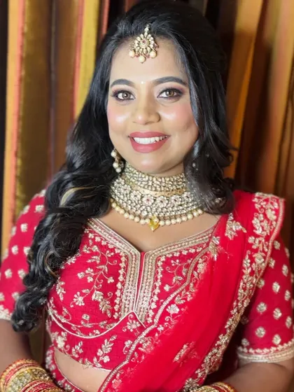 A close-up of this beautiful reception look. The focus is on a flawless, radiant complexion with a classic red lehenga and gold jewelry, a timeless combination for any bride.