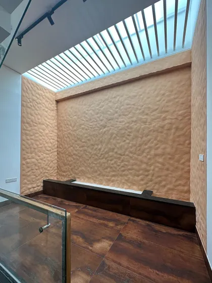A skylight with metal louvers illuminates a textured feature wall, demonstrating how we use overhead lighting to add depth and drama to a space.