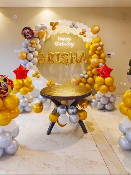 A classic Mickey Mouse themed birthday decoration. This setup uses a gold, silver, and white color scheme with a balloon ring, Mickey Mouse foil balloons, and personalized name balloons.