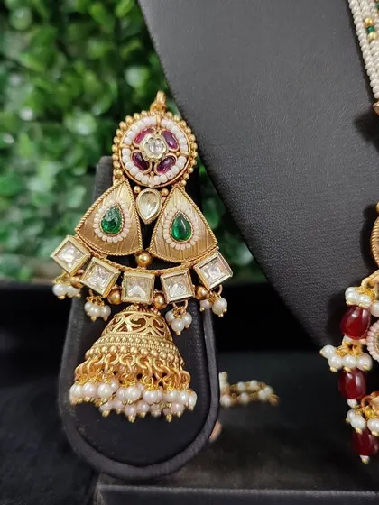 A close-up of an earring from the bridal set in image 147. The triangular design with kundan and green stones is both unique and traditional.