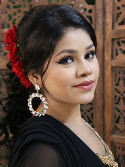 A classic party look with a winged eyeliner, soft pink lips, and a beautiful side-swept hairstyle adorned with red flowers. This is a versatile look suitable for many occasions.