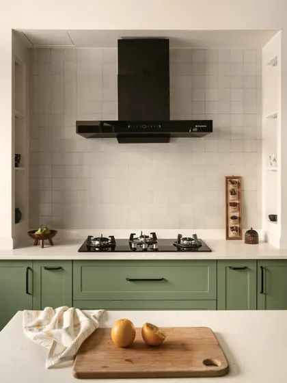 The kitchen features a hooded cooktop area with handy niches for cooking essentials. The sage green shaker-style cabinets and handmade-look tiles create a modern yet timeless feel.