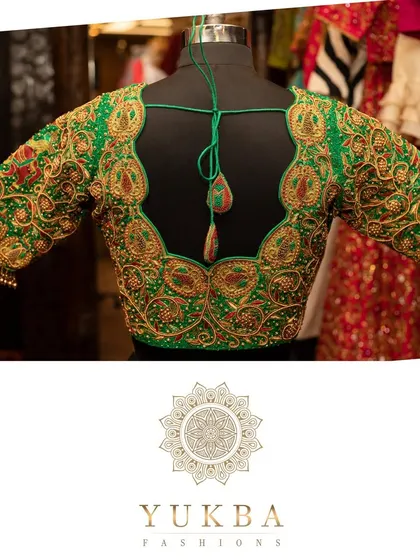 An emerald green blouse designed for a grand bridal look. The deep U-back is framed with heavy gold zardosi and resham embroidery, creating a piece that is both luxurious and unforgettable.