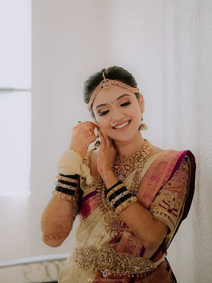 A candid moment of a bride adjusting her earring, with her perfectly draped saree providing an elegant backdrop. I focus on both beauty and comfort.