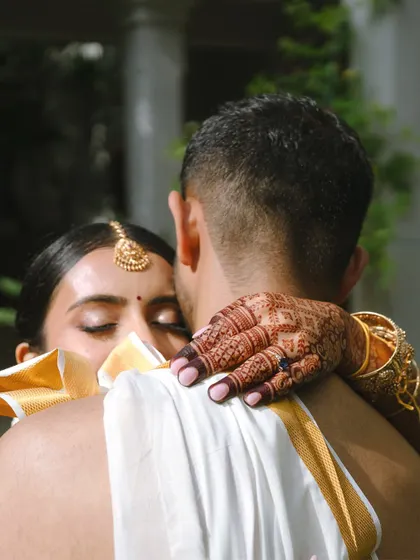 A close-up of the bride's henna-adorned hand as she embraces her groom, a beautiful and intimate detail.