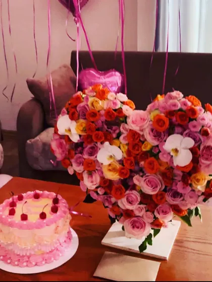 Perfect for anniversaries or a grand romantic gesture, this heart-shaped arrangement is overflowing with a mix of colorful roses and orchids. It’s designed to be a stunning centerpiece, shown here next to a birthday cake to complete the celebration.