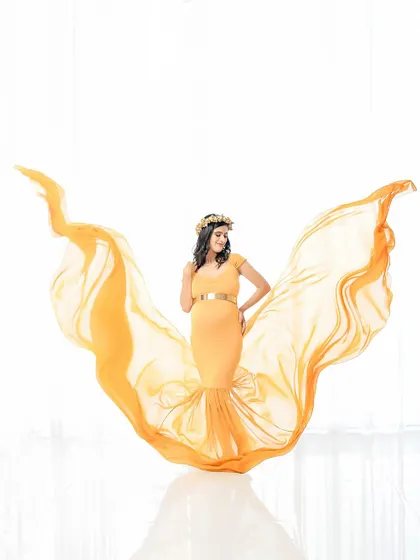 A stunning solo portrait featuring a flowing yellow gown with fabric tossed to create a wing-like effect. The bright white background makes the color pop, creating a joyful and energetic image.