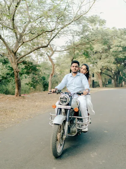 A cool and casual pre-wedding shot of a couple riding a motorcycle down a tree-lined road, capturing a sense of adventure and shared journey.