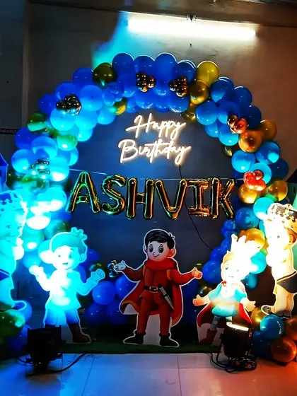 A royal first birthday for a little prince. The decoration features a castle-themed backdrop, a blue and gold balloon arch, and a light-up marquee number '1'.