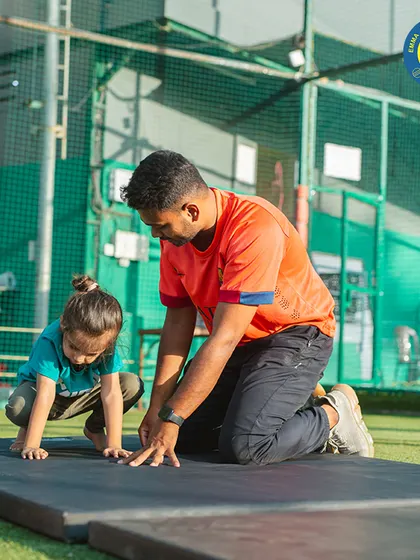 A coach guides a very young gymnast through the beginning stages of a forward roll, emphasizing safety and proper form from day one.