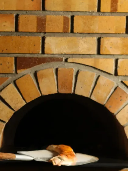 A pizza being carefully removed from our brick wood-fired oven. This traditional cooking method is key to achieving the perfect crispy crust and smoky flavour.