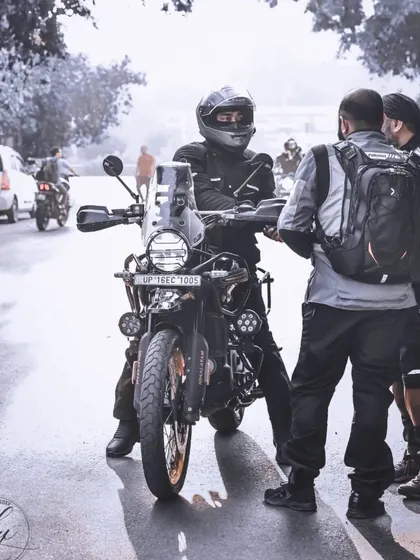 An atmospheric shot of riders conversing on a misty morning. The lighting and composition create a moody, cinematic feel that evokes the feeling of an early start to a long ride.