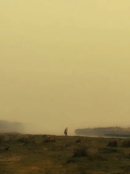 A highly minimalist and moody shot of a lone figure standing in a vast, hazy landscape. The yellow, foggy tones and the smallness of the person create a feeling of isolation and mystery.