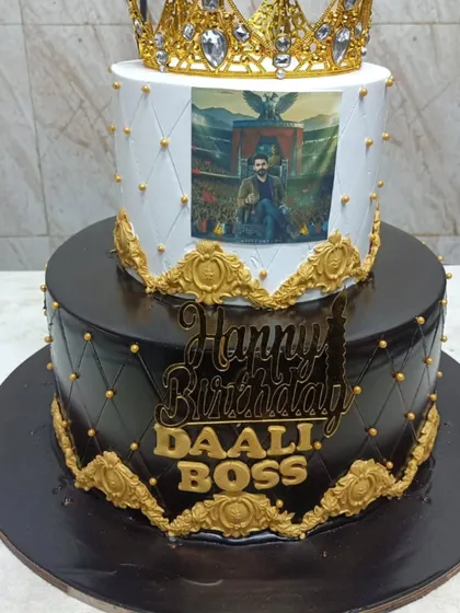 A crown, printed portrait and gold details finish our two-tier birthday cake, with white above a black lower tier.