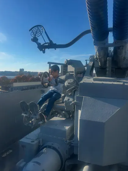 My son at the helm of an anti-aircraft gun on the deck of the USS Intrepid. Interactive exhibits like this make history come alive and give children a tangible connection to the past.