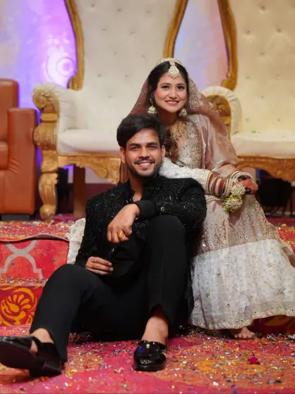 A stylish and relaxed portrait of the couple after their ceremony, seated amidst confetti. The groom's modern black sherwani complements the bride's traditional attire.