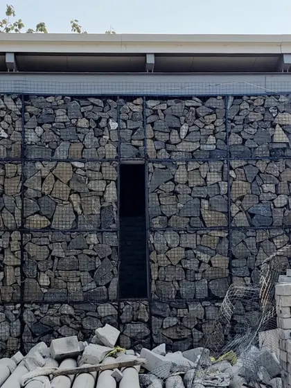 A narrow, monolithic doorway is carved into a massive gabion wall at our Alibaug project. This creates a sense of mystery and passage, contrasting the solid, heavy wall with the dark, inviting void.