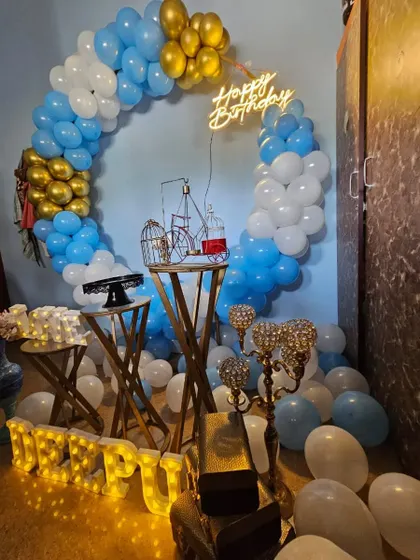A full view of the blue, white, and gold balloon decoration, perfect for a birthday or anniversary celebration at home. The light-up name 'Deepu' adds a personal touch.