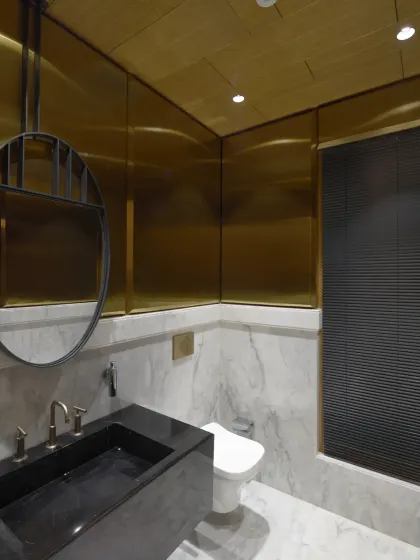 This bathroom in the Screen House exudes luxury with its black, white, and gold palette. A sleek round mirror and opulent golden accents on the walls and ceiling add a touch of sophisticated glamour.