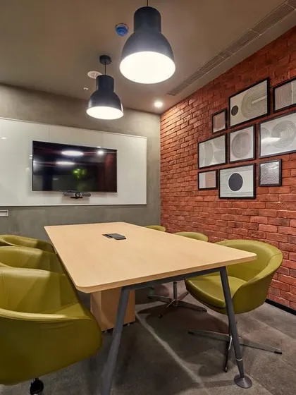 An intimate meeting room with an exposed brick wall and comfortable green armchairs. The space feels more like a cozy study than a corporate meeting room.