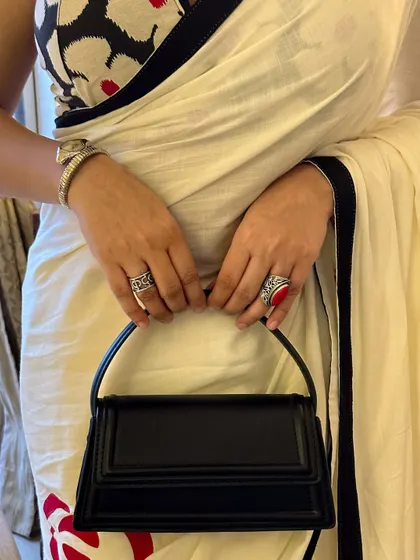 A close-up on the accessories. The structured black bag, silver watch, and statement rings add layers of texture and personality to the hand-painted saree look.