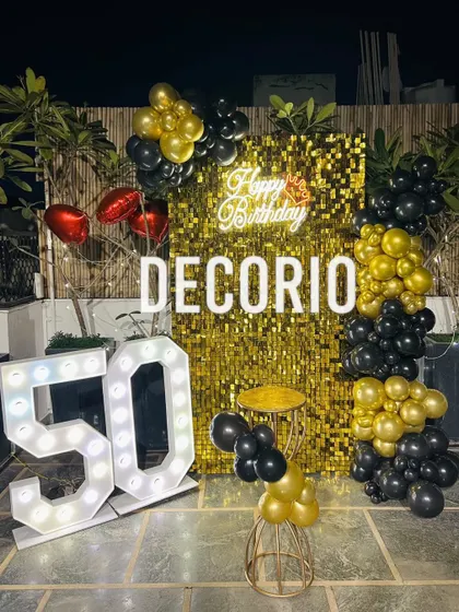 A spectacular 50th birthday party on a terrace, designed for a memorable night-time celebration. This setup features a brilliant gold sequin backdrop, a custom neon sign, large light-up '50' marquee numbers, and a dramatic black and gold balloon arrangement.