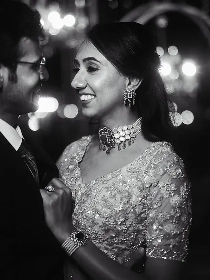 A classic black and white reception portrait. The joy in their expressions and the sparkling lights in the background create a timeless image of celebration.