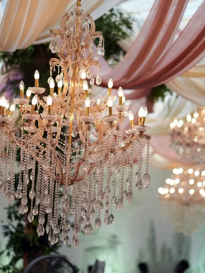 A close-up of the stunning crystal chandeliers hanging amidst draped pastel fabrics. The warm light from the bulbs creates a romantic and celebratory glow.