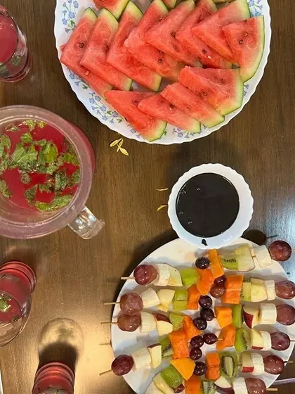 A simple yet elegant way to enjoy fruits. This platter includes fresh fruit skewers with a chocolate dip, sliced watermelon, and a refreshing mint-infused drink. It's a perfect healthy dessert or snack option.