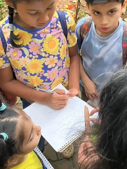 A group of children collaborates on a nature journaling entry, discussing their observations and documenting them together.