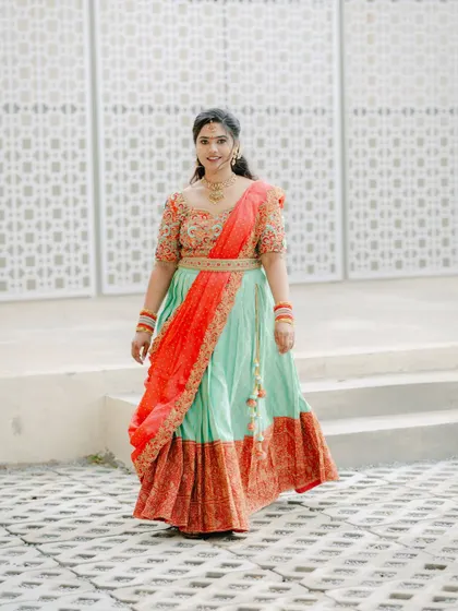 A full-length shot of a bride in a beautiful mint and red lehenga, walking with a graceful smile.