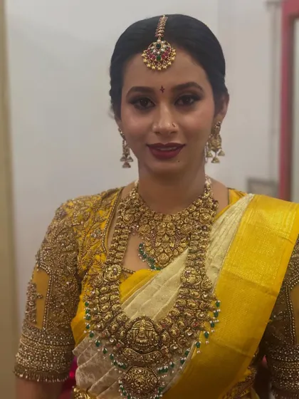 A portrait of a bride in a yellow silk saree, her hair neatly styled to showcase her intricate temple jewellery.