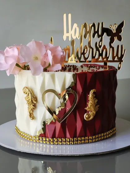 This anniversary cake features a striking two-tone design with a geometric, origami-style texture on the bottom tier. The clean lines and bold color contrast create a modern and sophisticated look.