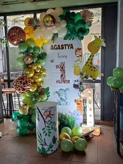 A jungle-themed first birthday perfect for smaller spaces. This setup includes a custom backdrop, a green and gold balloon arch, and a light-up number '1'.