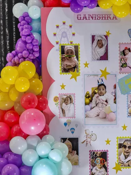 A close-up of a milestone board from a carnival-themed first birthday. The board is decorated with photos from the baby's first year, surrounded by colorful balloon art.