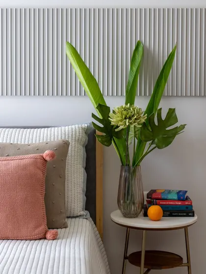 A detail from a bedroom where a fluted panel headboard in a soft grey is paired with a marble side table and blush pink pillows.
