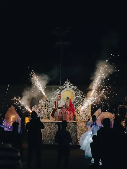A grand, theatrical entry for the couple on their wedding day. This shot captures the scale of the celebration, with the couple seated on a magnificent throne-like structure, surrounded by performers and fireworks.