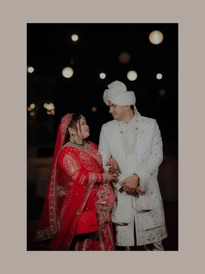 A classic wedding portrait. The couple shares a loving glance under the warm glow of decorative lights, a timeless and romantic shot.