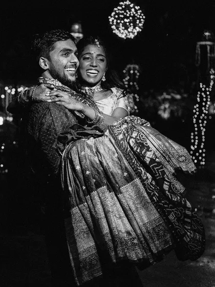 A fun and energetic black and white shot of the groom lifting his bride at night. The candid joy and the sparkling lights in the background make this a magical, memorable moment.