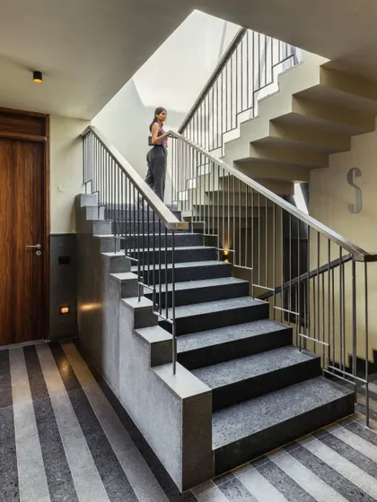 The central staircase is flooded with natural light from a skylight above, making the transition between floors a bright and pleasant experience. The simple steel railing and stone steps maintain the building's clean, modern aesthetic.
