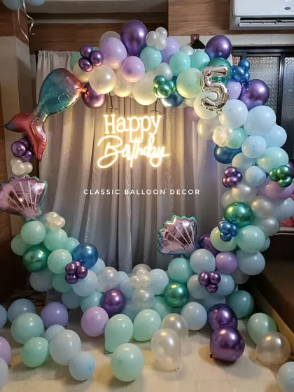 An enchanting Mermaid theme for a 5th birthday, featuring a balloon ring in ocean colors, a neon sign, and mermaid tail and seashell foil balloons.