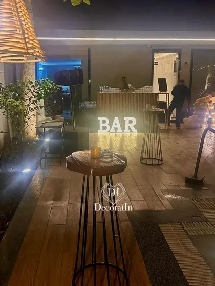 The bar area for the 40th birthday party, featuring a lit-up "BAR" sign and rustic high-top tables for a relaxed and social atmosphere.